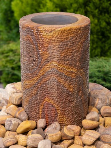 Cylindrical rainbow sandstone, water feature. Gentle cascades of water trickle down to the pebbles below.